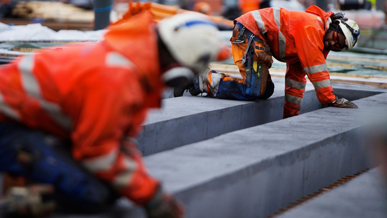 To mannlige fagarbeider som jobber med betong på en byggeplass